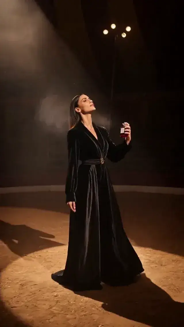 A crimson perfume bottle under a warm spotlight in a smoky dark-circus set